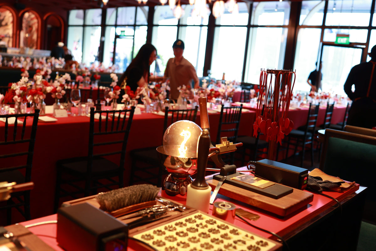 Live leather hot stamping and personalization pop-up booth set up inside an elegant dining venue for Dior Lucky Red event with red tablescapes.